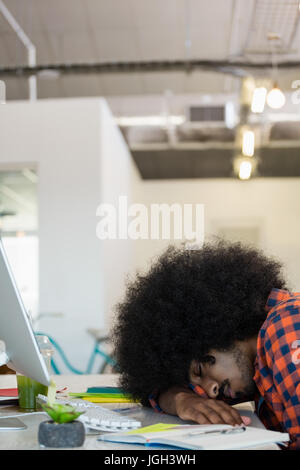 Tired young man with curly hair sleeping at desk in creative office Stock Photo