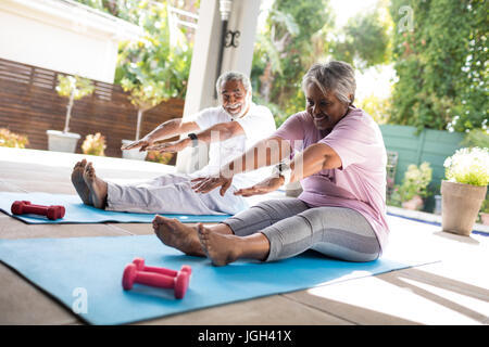 Full length of senior couple doing stretching exercise while sitting on exercise mat in yard Stock Photo