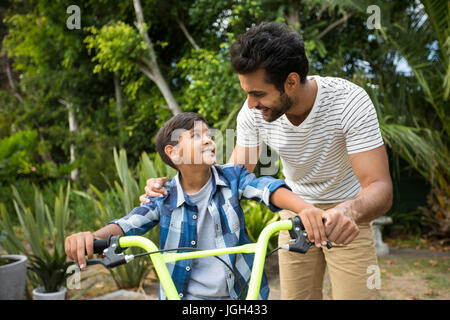 Father and son standing in yard with bicycle while looking at each other Stock Photo