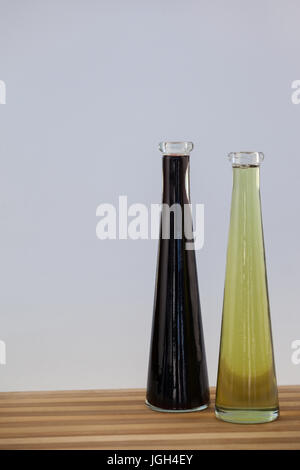 Black and green olive oil in bottle on wooden table against wall Stock Photo