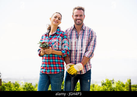 Portrait of smiling woman with man holding potted plant against sky at lawn Stock Photo