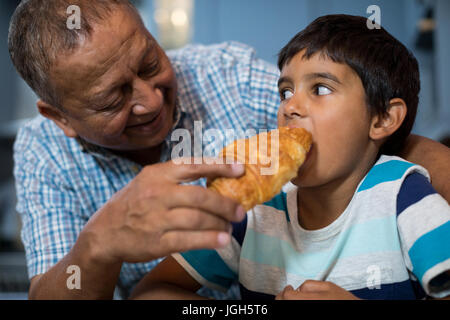 Grandfather feeding croissant to grandson while having breakfast Stock Photo