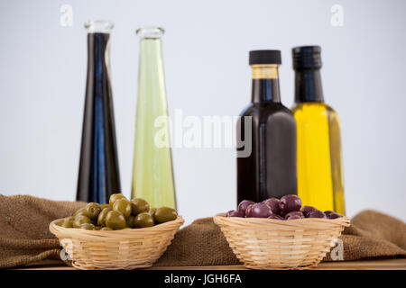 Olives in wicker basket with oil bottle on table against wall Stock Photo