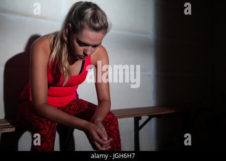 Sad woman relaxing on bench in fitness studio Stock Photo