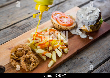 High angle view of bottle pouring mustard sauce on French fries by burger ingredients Stock Photo
