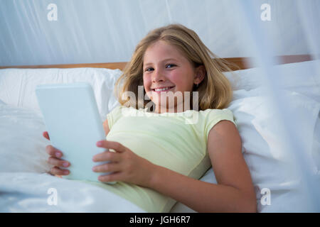 Portrait of girl holding tablet computer while lying on bed in bedroom at home Stock Photo