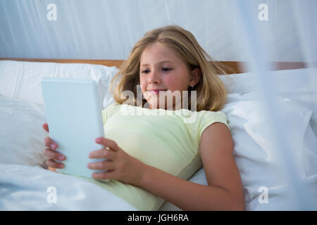 Girl using tablet computer while lying on bed in bedroom Stock Photo