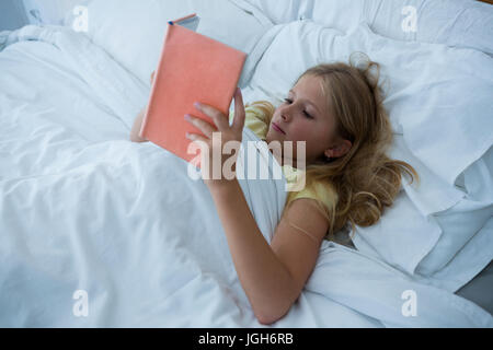 High angle view of girl reading book while lying on bed at home Stock Photo