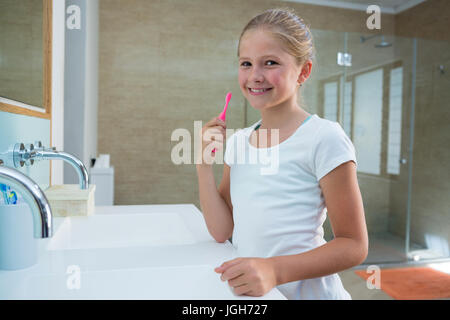 Portrait of girl holding toothbrush while standing in bathroom Stock Photo