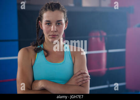 Portrait of confident young female athlete with arms crossed against boxing ring at fitness studio Stock Photo