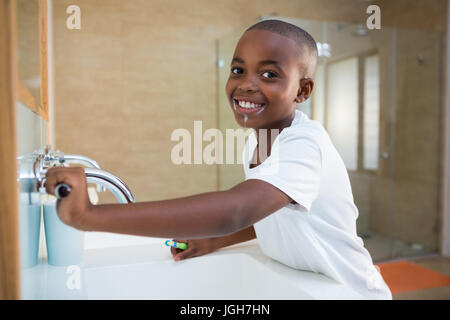 Side view portrait of smiling boy with toothbrush looking at mirror in domestic bathroom Stock Photo