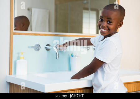 Side view portrait of smiling boy washing hands in sink at domestic bathroom Stock Photo