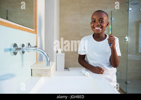 Portrait of smiling boy showing toothbrush while standing by sink at bathroom Stock Photo