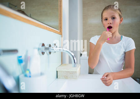 Portrait of girl brushing teeth while standing by sink in bathroom Stock Photo