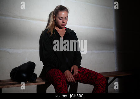 Sad woman relaxing on bench in fitness studio Stock Photo