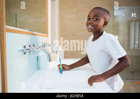 Portrait of smiling boy standing by sink with toothbrush at domestic bathroom Stock Photo