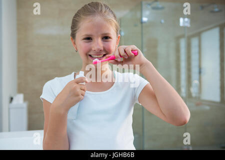 Portrait of girl brushing teeth while standing in bathroom Stock Photo