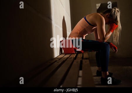 Sad woman sitting on bench in fitness studio Stock Photo