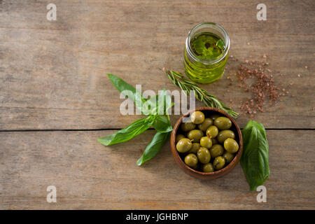 Close-up of marinated green olives in bowl and oil container with green leaf on table Stock Photo
