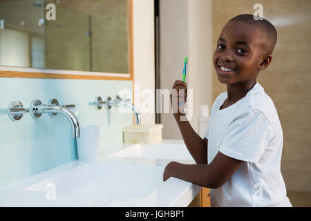 Side view of portrait of smiling boy with toothbrush standing in bathroom Stock Photo