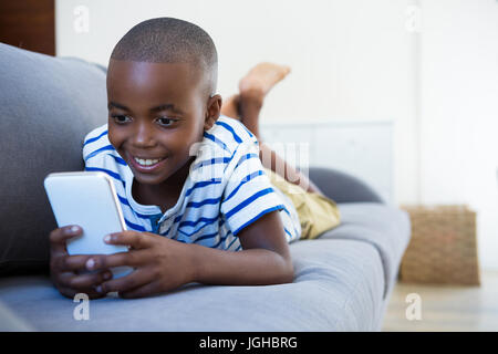 Smiling boy using mobile phone while lying on sofa in living room at home Stock Photo