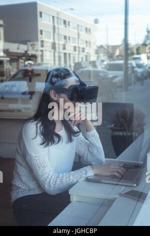 Woman using laptop and virtual reality headset in the restaurant Stock Photo