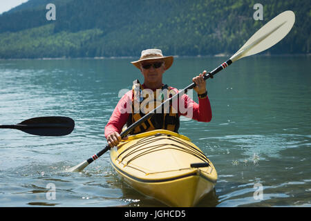 Man in life jacket oaring while kayaking over lake Stock Photo