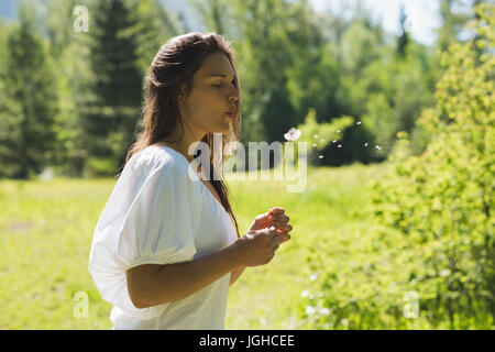 Beautiful woman blowing dandelion in park on a sunny day Stock Photo