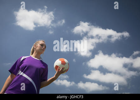 Low angle view of young woman holding soccer ball against sky Stock Photo