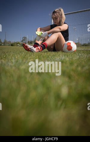 Full length of tired female soccer player sitting by goal post on field Stock Photo