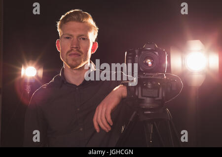 Portrait of photographer standing by camera at illuminated studio Stock Photo