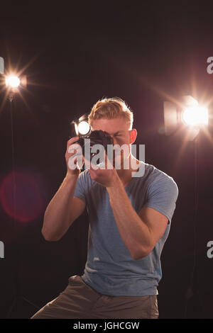 Male photographer photographing from camera at illuminated studio Stock Photo