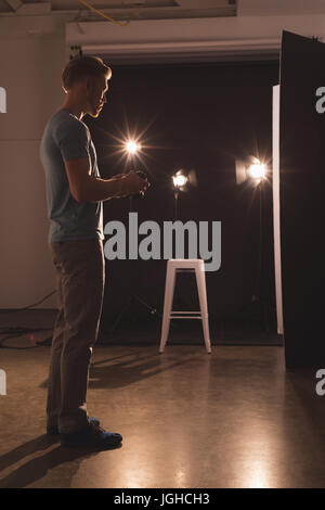 Side view full length of photographer holding camera at illuminated studio Stock Photo