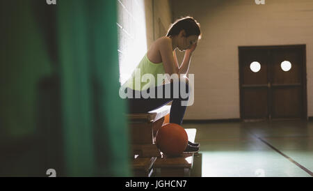 Side view of female basketball player sitting on bench in locker room Stock Photo