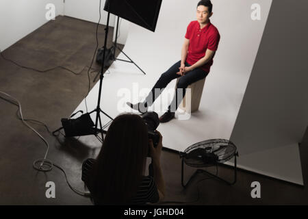 Female photographer photographing young man posing at studio Stock Photo
