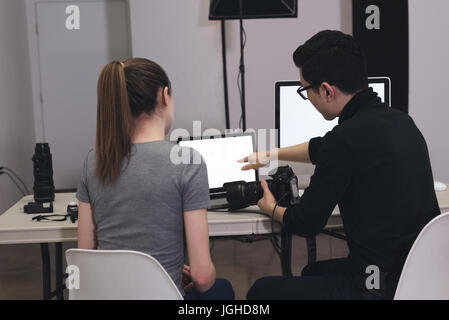 Male photographer explaining assistant while using laptop at studio Stock Photo