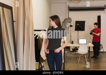 Young female model looking into mirror with photographer holding camera at studio Stock Photo