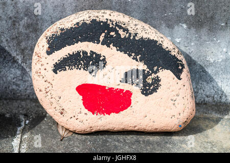 Stone propped against wall of local school with human face painted on. Stock Photo