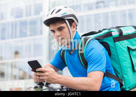 Courier On Bicycle Delivering Food In City Using Mobile Phone Stock Photo