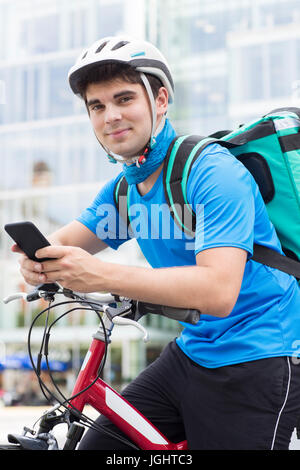 Courier On Bicycle Delivering Food In City Using Mobile Phone Stock Photo