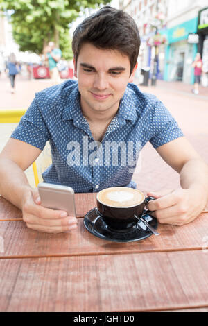 Young Man At Outdoor Cafe Texting On Mobile Phone Stock Photo