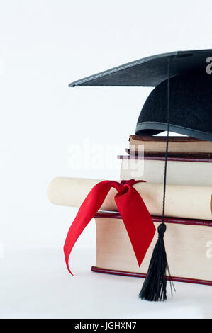 A graduation mortarboard on top of a stack of books, with parchment scroll tied in red ribvon. Stock Photo