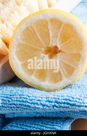 Close up of half a lemon, facing front, piled together with a wooden bristle scrubbing brush and a microfibre cloth to represent natural, non-toxic cl Stock Photo