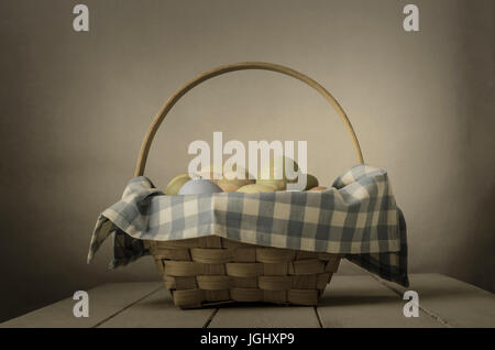 Woven wicker handled basket lined with gingham check fabric and filled with hand painted Easter eggs on top of an old, shabby painted white farmhouse  Stock Photo