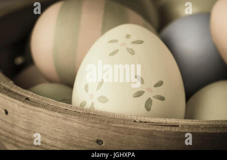 Close up of hand painted Easter eggs piled in a wicker basekt.  Striped and plain varieties in background with pale yellow and green floral egg in for Stock Photo