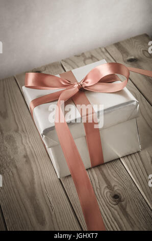 Angled shot of a gift box with closed lid, wrapped in silver paper and tied to a bow with a satin ribbon.  Placed on a weathered old wooden table. Stock Photo