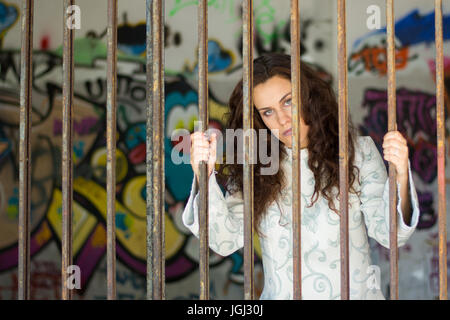 A long-haired and sad-looking woman behind bars Stock Photo