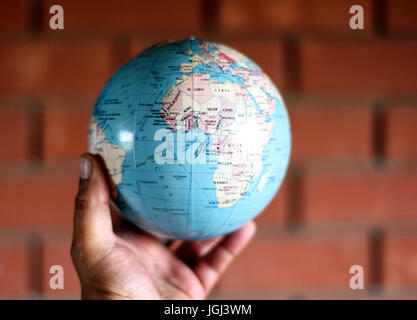Globe map of planet earth held by a human hand against a brick wall Stock Photo