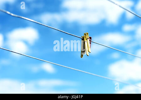 Three brightly colored plastic clothes pegs on a  family washing line with blue sky and white summer clouds in the background Stock Photo