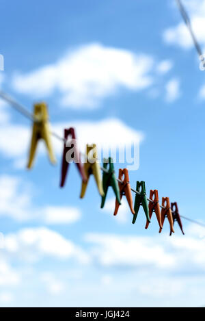 An assortment of brightly colored washing pegs and clothespins on a outdoor washing line with bright blue sky and white summery clouds Stock Photo
